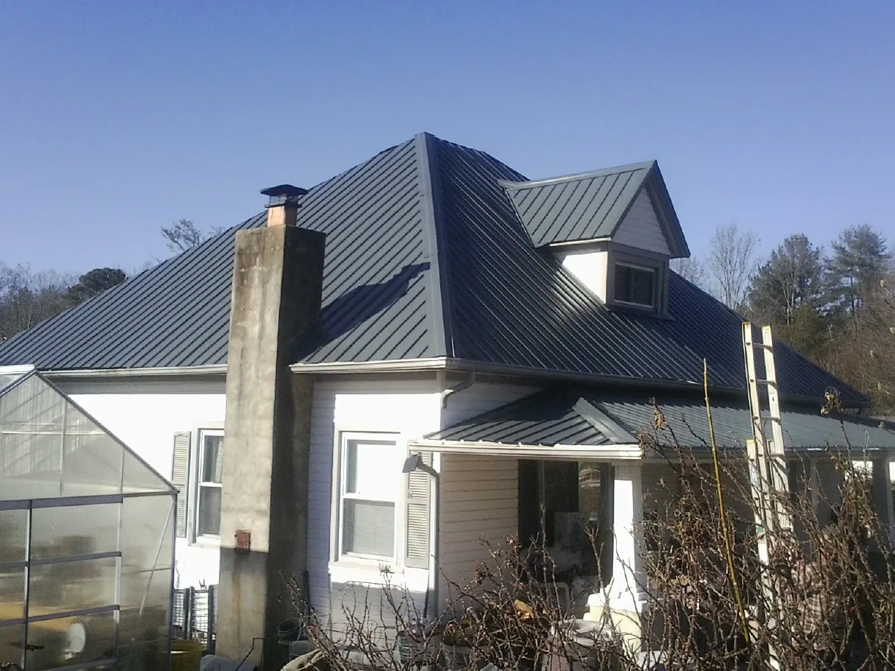 Dark blue standing seam metal roof on a white farmhouse with dormer — Slate & Tile Roof Repair by Roofing Brothers in Owosso