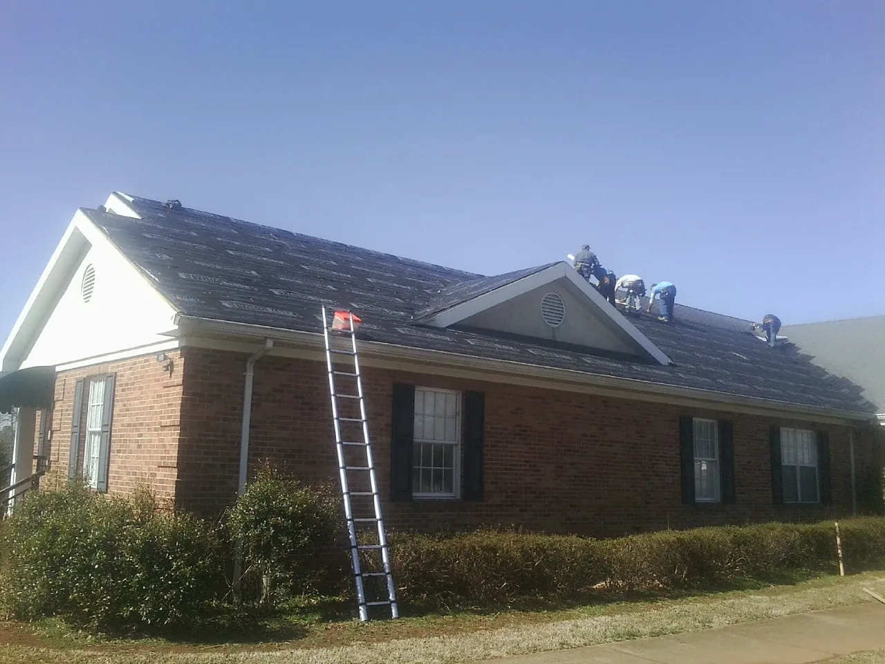 Crew tearing shingles off a brick ranch roof with a ladder set — Metal Roof Repair work by our crew in Owosso