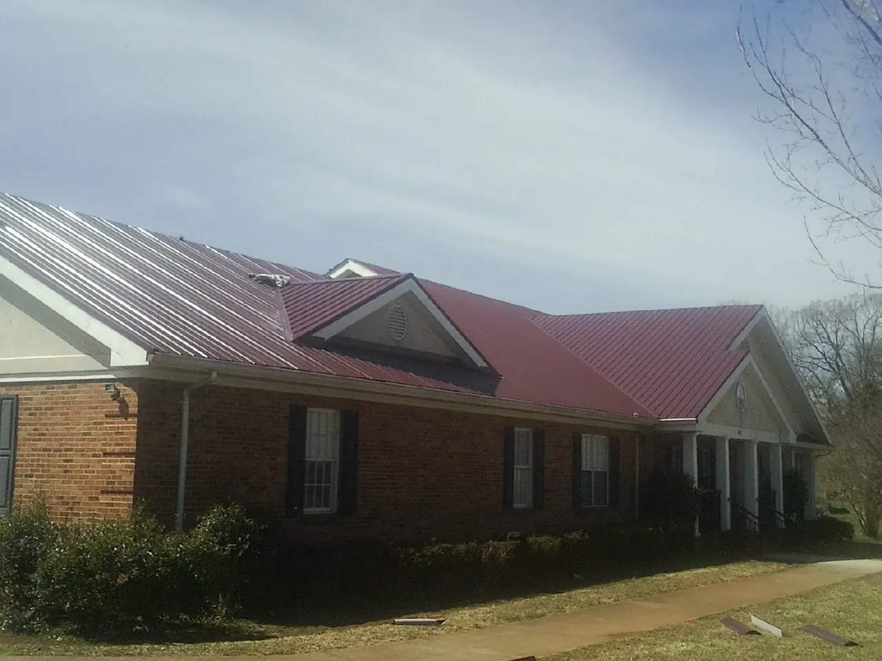Red metal roof with gabled entries on a long brick building, from a Hail Damage Roof Repair job in Owosso