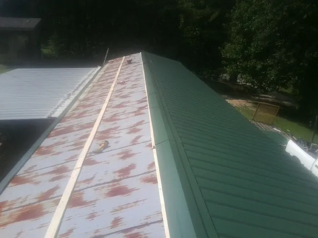 Old rusted panels beside newly installed green metal roofing — Wind Damage Roof Repair by Roofing Brothers in Owosso