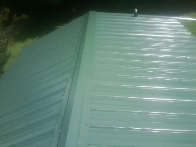 New green metal panels meeting at the ridge of a roof — Flat Roof Repair work by our crew in Owosso