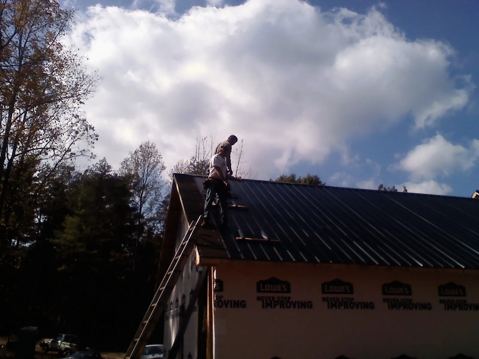 Roofer fastening dark metal panels high against a cloudy sky, from a Roof Inspection job in Owosso