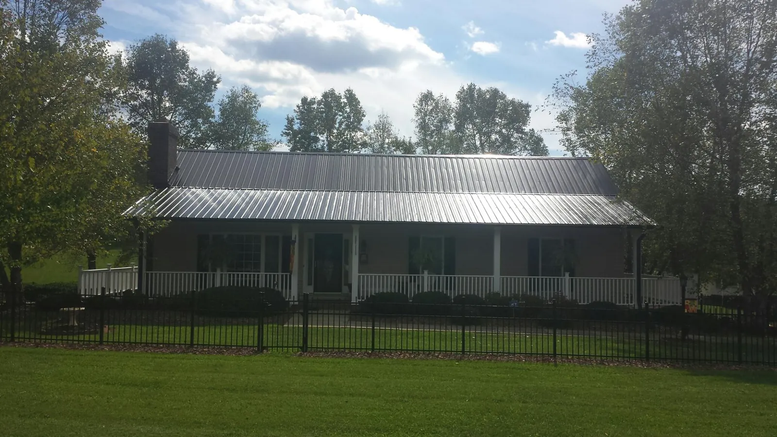 Gray metal roof on a brick ranch with a full width front porch — Gutter Guard Installation work by our crew in Owosso
