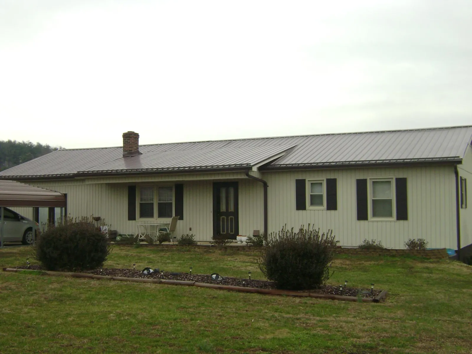 Brown metal roof on a cream sided ranch home with a brick chimney in Owosso