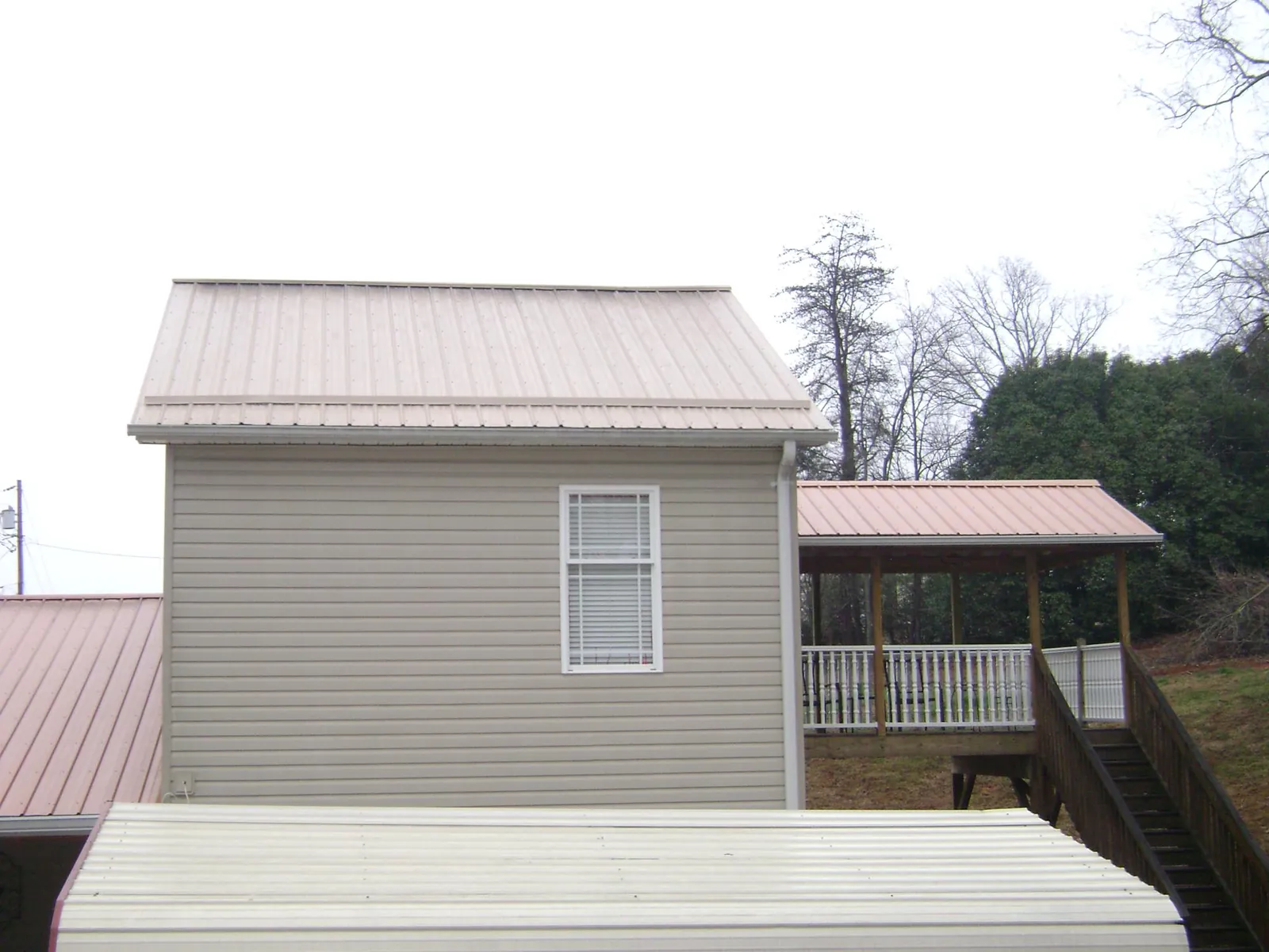 Tan metal roofs on a two story addition and attached porch, from a Roof Replacement job in Owosso